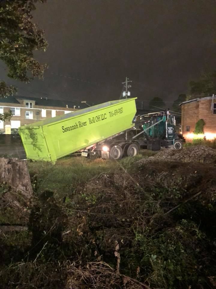 A dump truck is dumping dirt in a field at night.