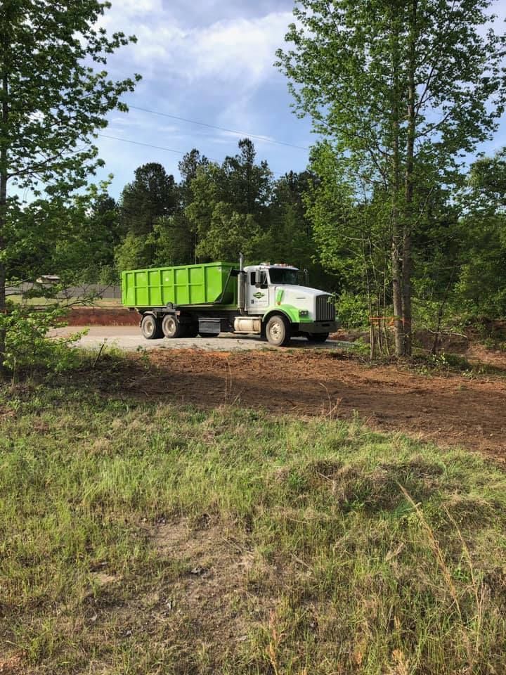 A green dump truck is driving down a dirt road.