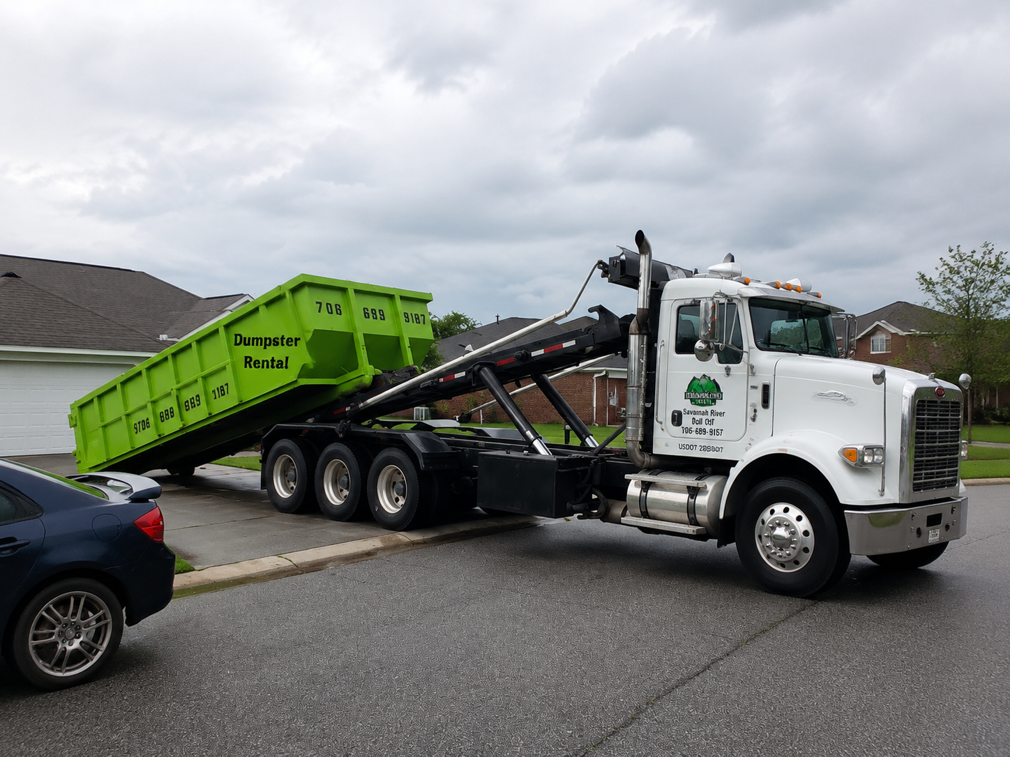 A green dumpster is being towed by a green dump truck.