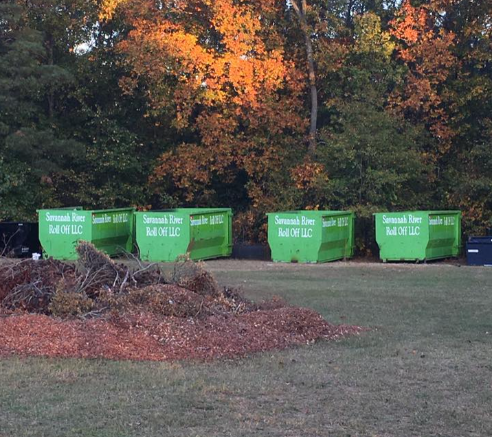 A row of green dumpsters are lined up in a field