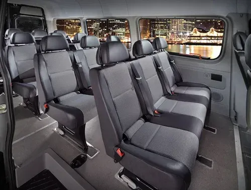 Interior of a passenger van with rows of gray seats and a nighttime city view out the windows.
