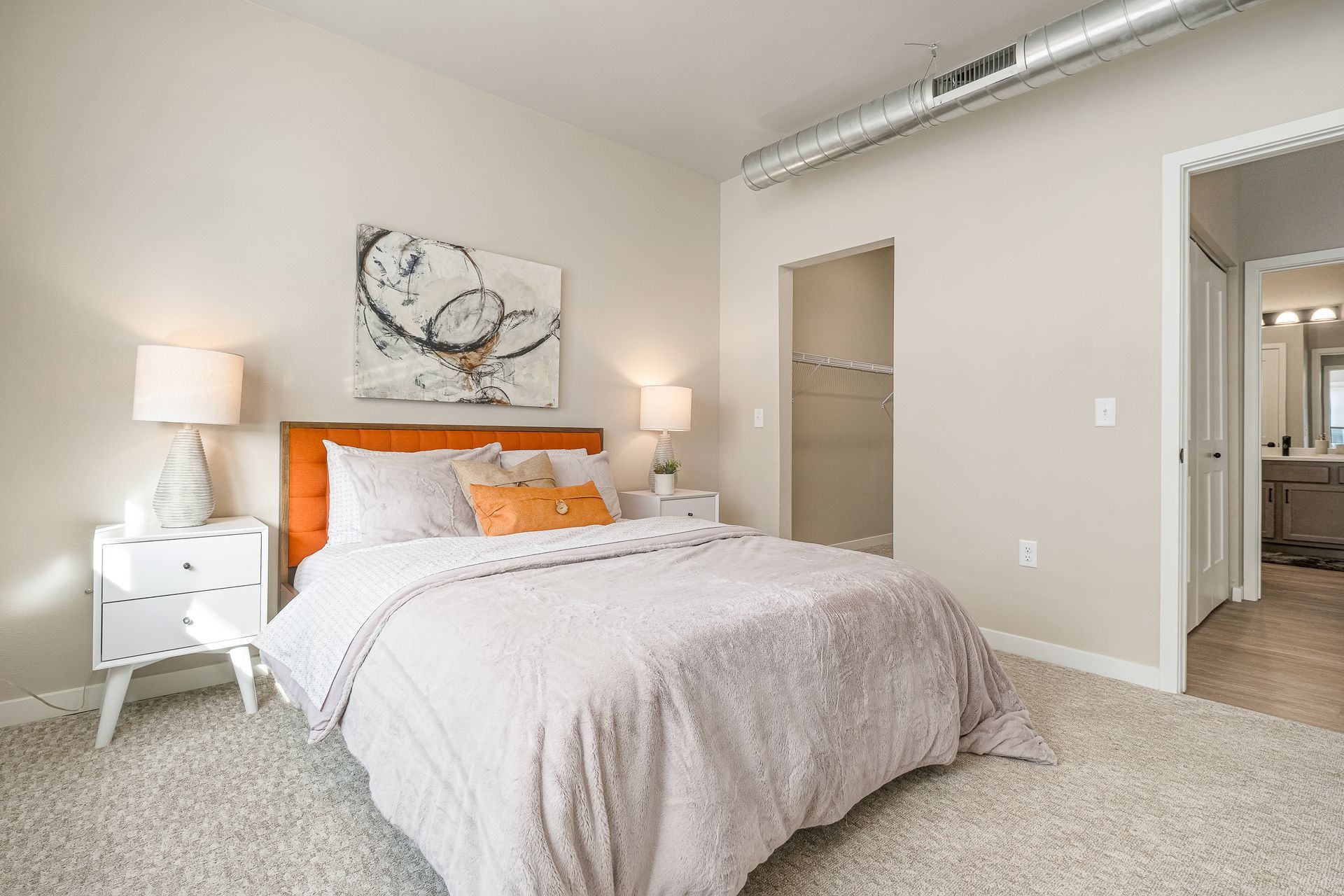 A bedroom with a bed , nightstands , lamps and a painting on the wall.