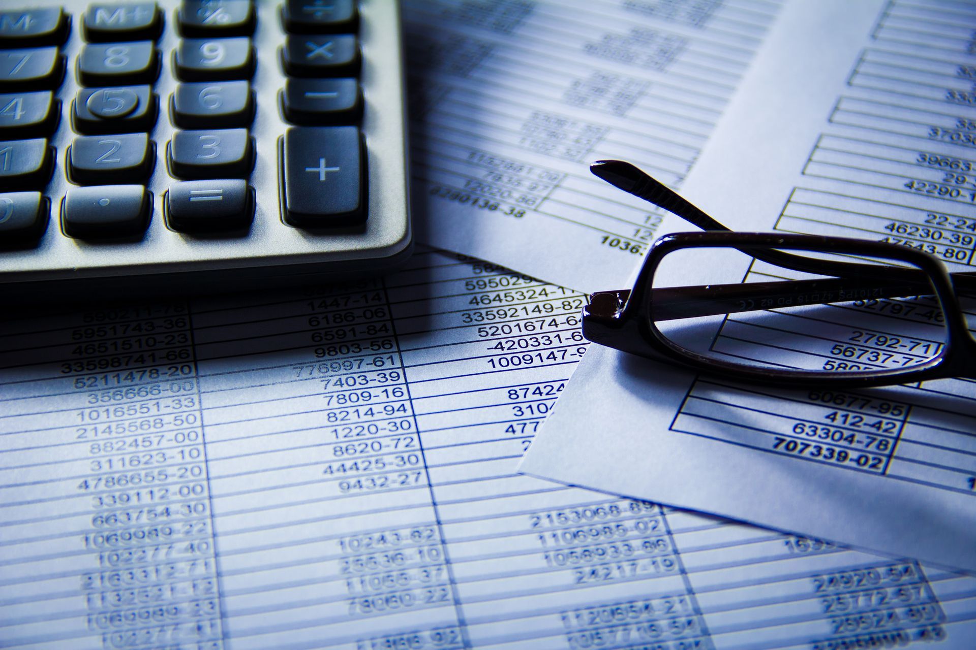 Calculator, eyeglasses, and financial documents with numbers.
