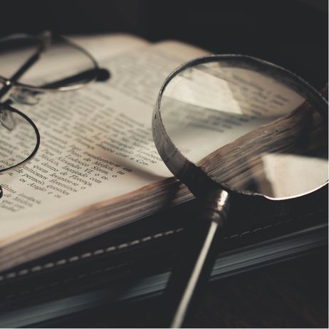Magnifying glass over an open book with glasses resting on it.