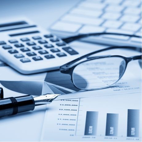 Calculator, glasses, pen, and keyboard on top of financial graphs.