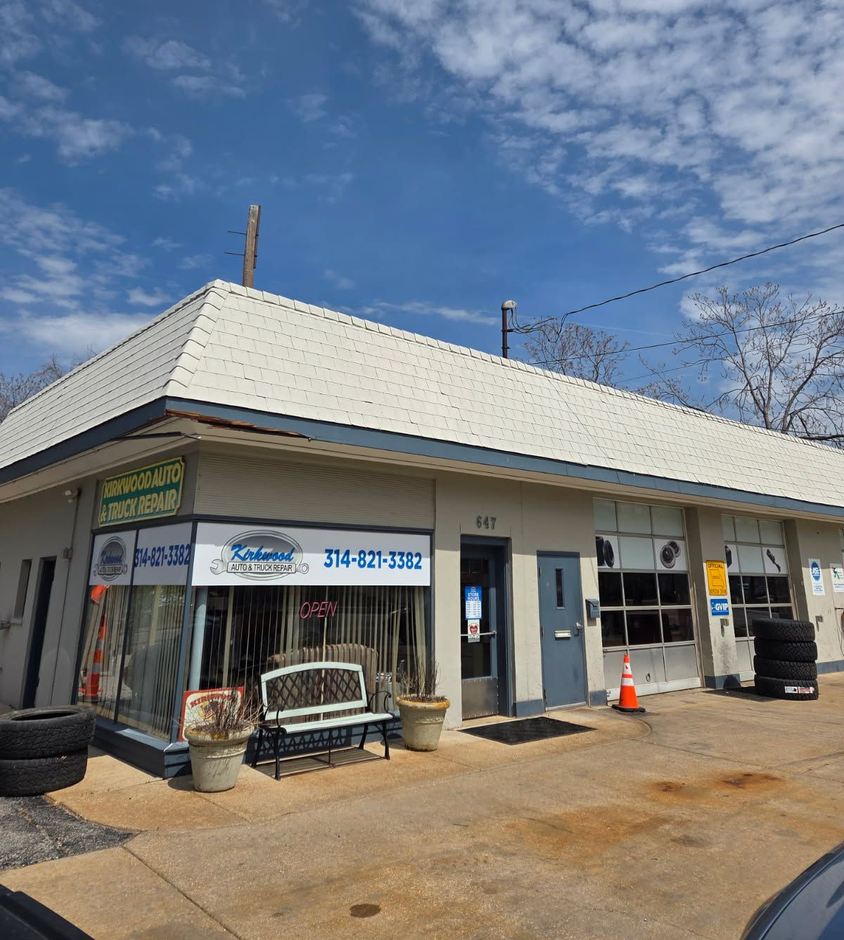 A tan-colored auto and truck repair shop with a white shingled roof, large front windows, and a paved lot.