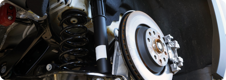 Close-up of a car's rear suspension, showing the coil spring, shock absorber, and brake disc assembly.