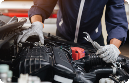 A mechanic wearing work gloves works on an open car engine, holding a wrench.
