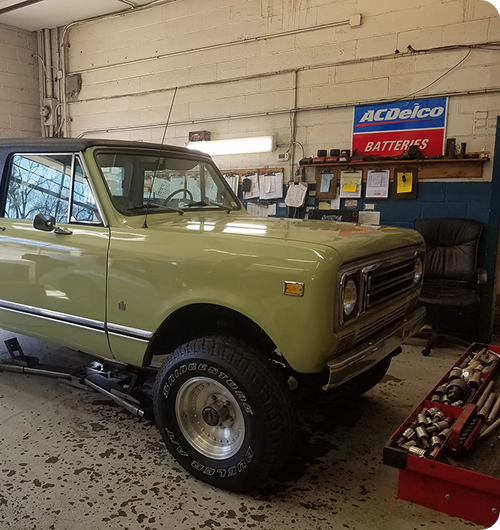 A light green International Harvester Scout parked inside a workshop with a black roof and off-road tires.
