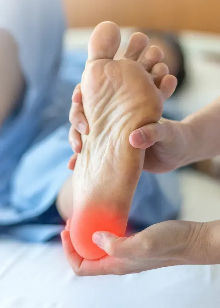 A hand holds a foot, with a red highlighted area indicating pain on the heel.