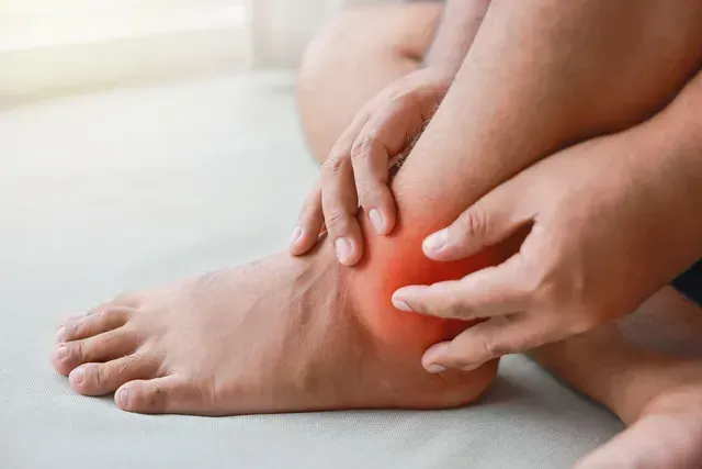 Hands holding a swollen, red, and painful-looking ankle, highlighting localized discomfort and inflammation.