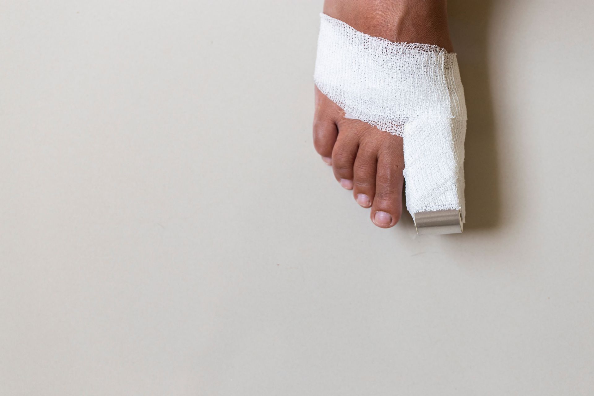 A bare foot with the big toe wrapped in a white bandage or cast against a plain, light-colored background.
