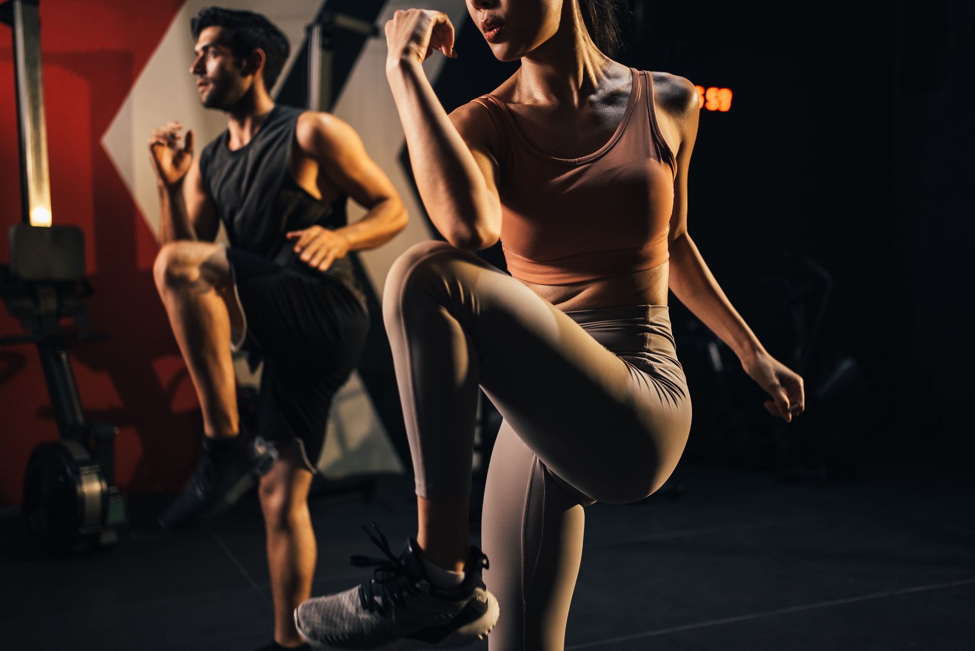Two people exercising in a dark gym, one lifting a knee and the other stepping in place.