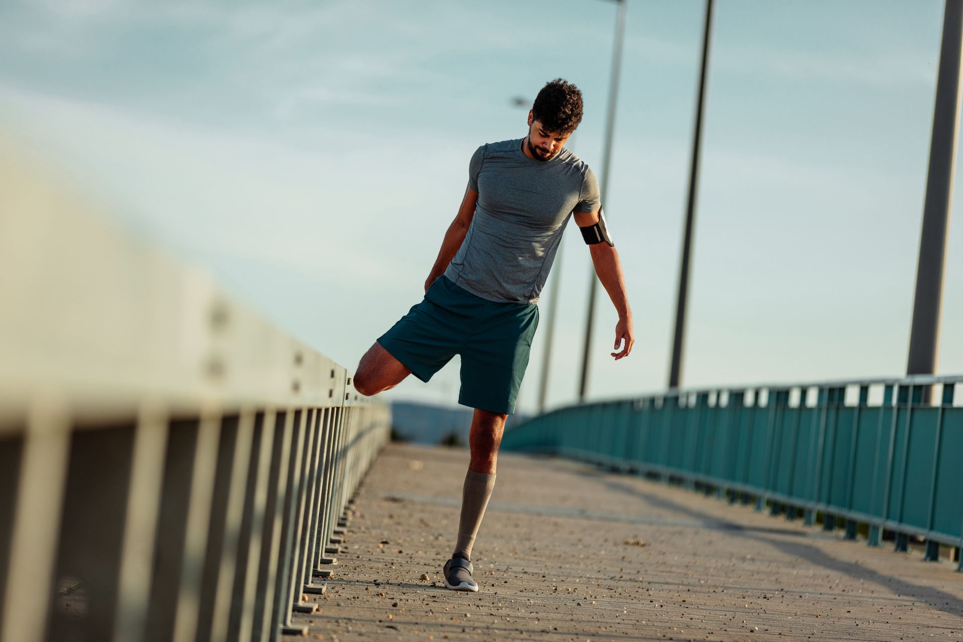 Man balancing on one leg on a bridge, with railings and open sky in the background