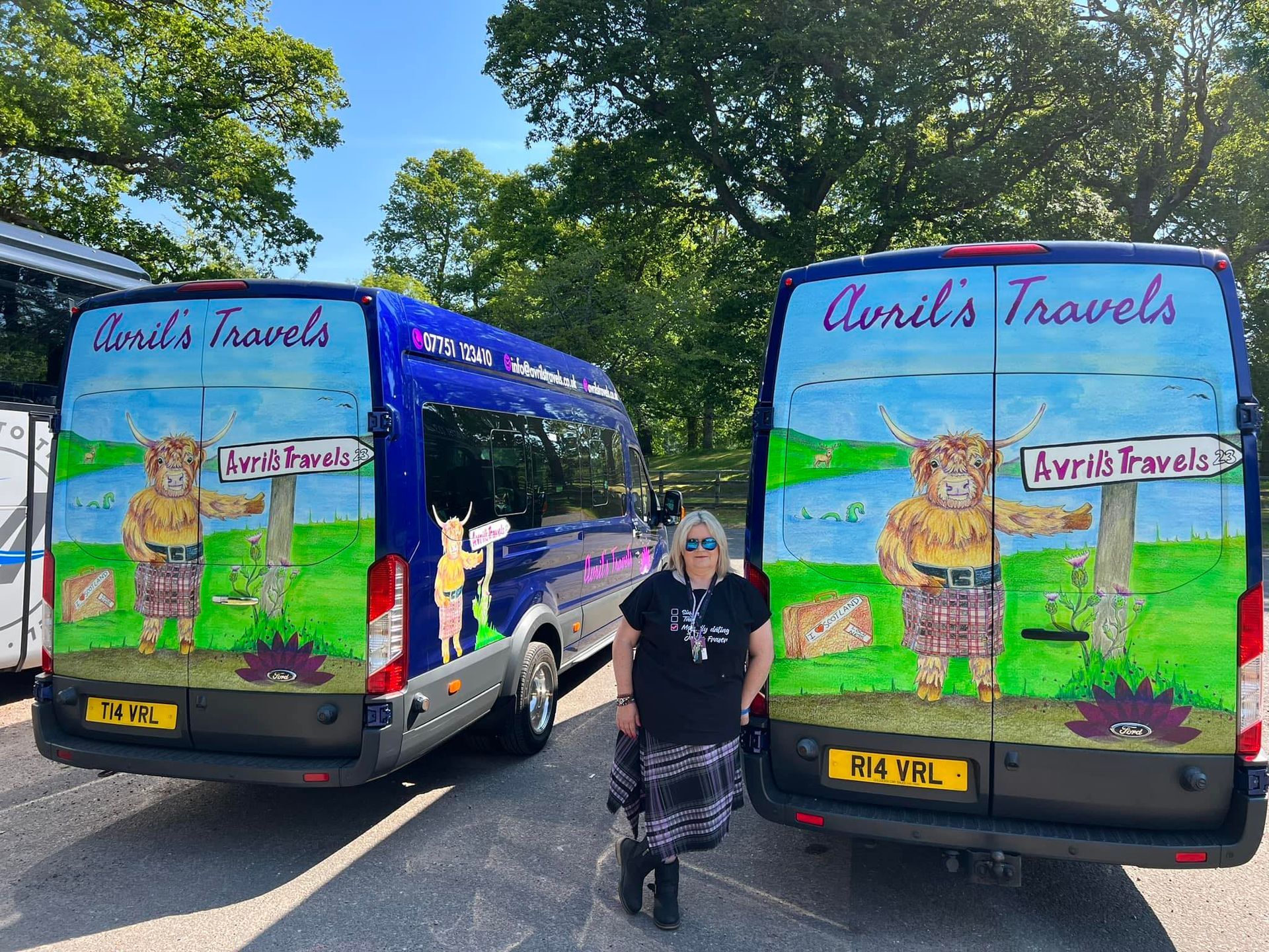 A woman is standing in front of two vans painted with scottish animals.