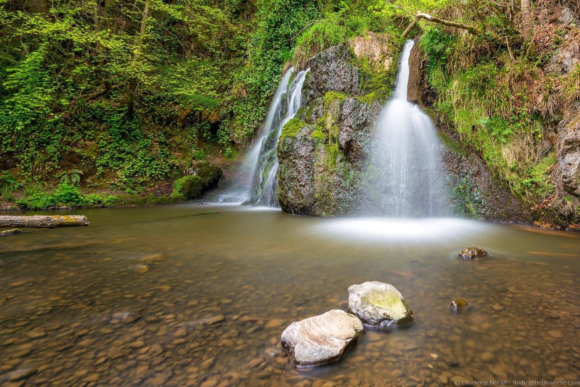 A waterfall is surrounded by rocks and trees in the middle of a river.