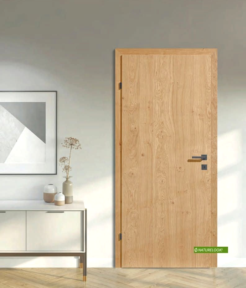 Stanza minimalista con porta in legno chiaro e un tavolino accanto a un quadro incorniciato appeso alla parete.