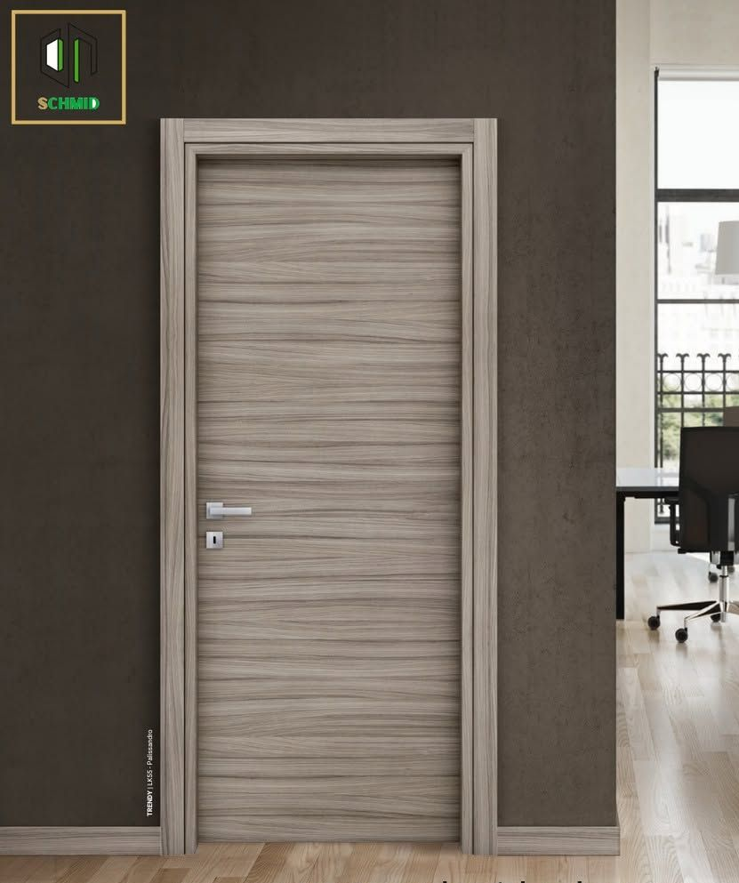 Porta d'ufficio in legno con maniglia argentata in un corridoio moderno, con uno scorcio dello spazio di lavoro al di là.