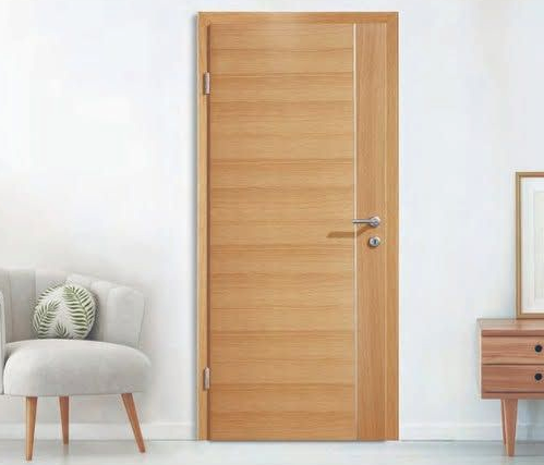 Una porta interna in legno chiaro è posizionata al centro tra una sedia grigia e un tavolino in legno in una stanza luminosa.