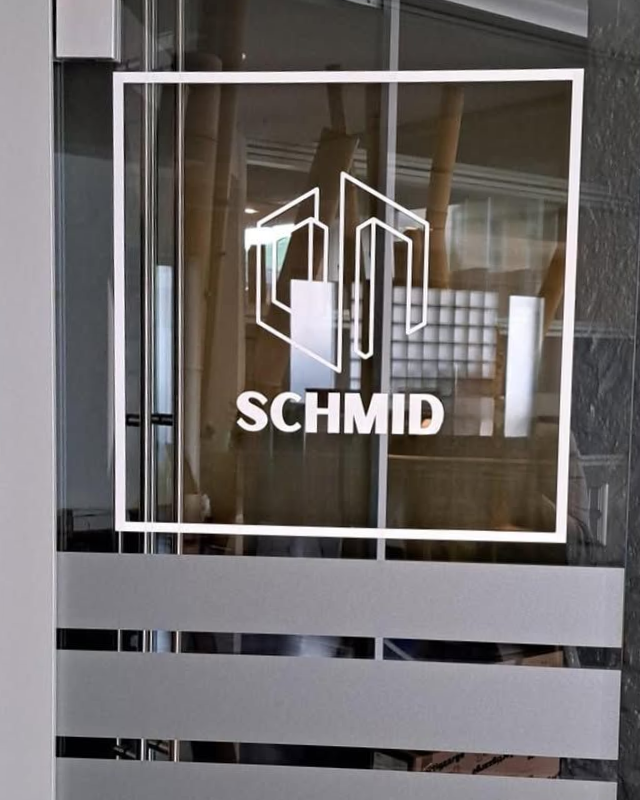 Porta in vetro con logo SCHMID bianco ed emblema geometrico sopra strisce orizzontali satinate.