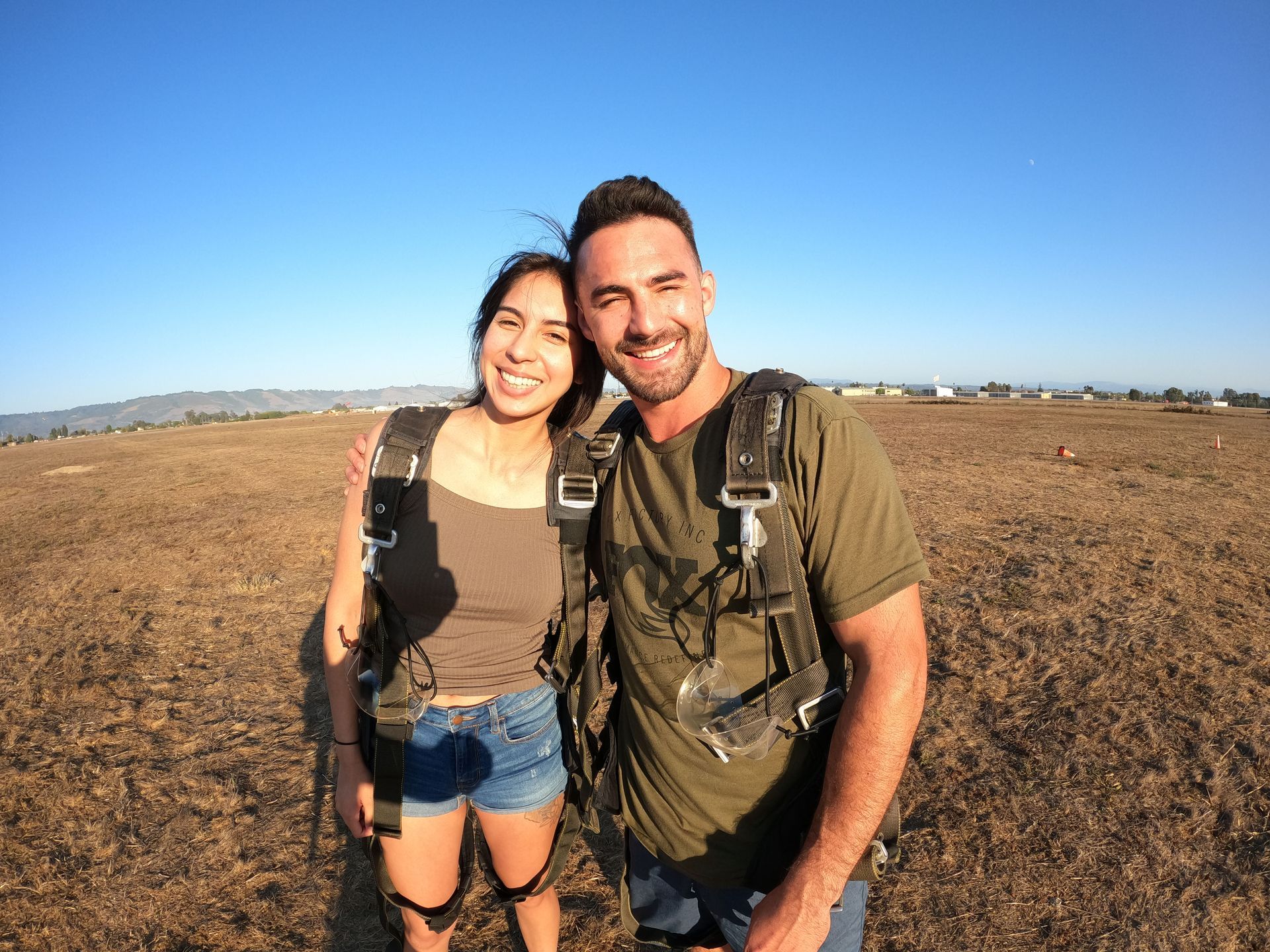 A man and a woman are pose for a picture in a field after landing from a tandem skydive at Skydive Santa Cruz