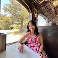 A woman in a pink dress is sitting at a table with a glass of wine.