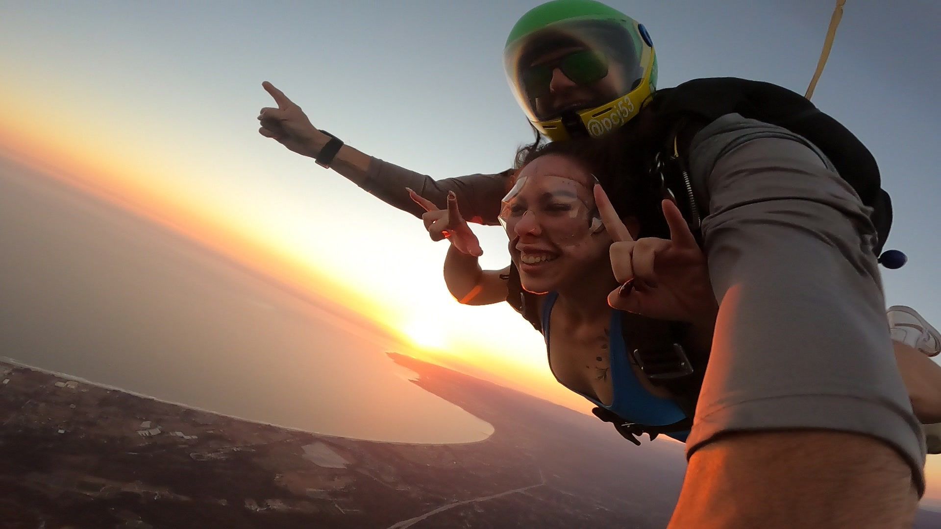 Tandem Skydive pair freefall through the air at sunset overlooking the Pacific Ocean.