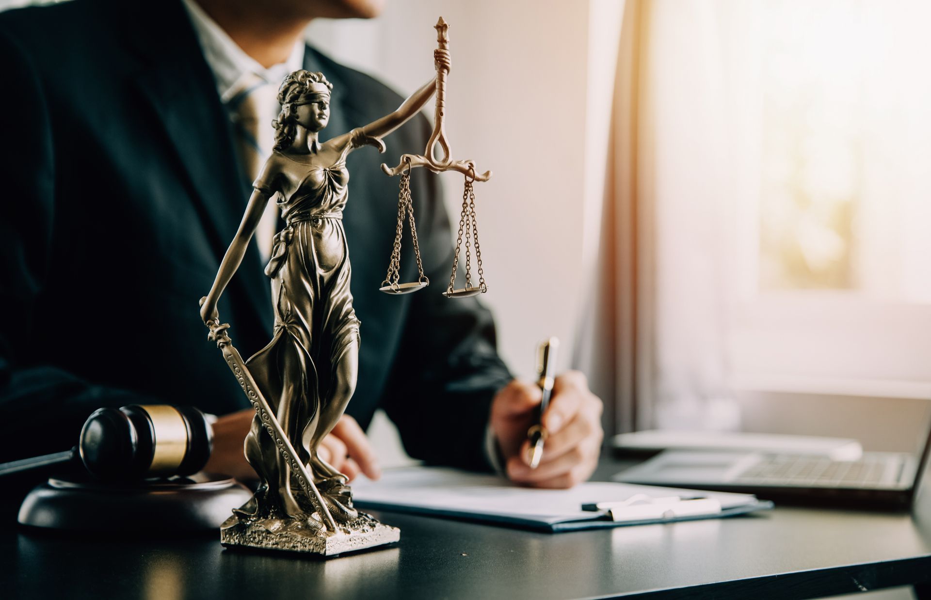 A Man in a Suit is Sitting at a Desk With a Statue of Justice