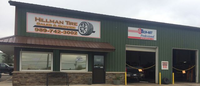 A green metal building with a sign for Hillman Tire and an open garage bay. | Hillman Tire Sales and Service LLC