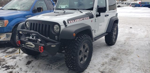 A white Jeep Wrangler Rubicon with a black aftermarket bumper and off-road tires parked on a snowy lot. | Hillman Tire Sales and Service LLC