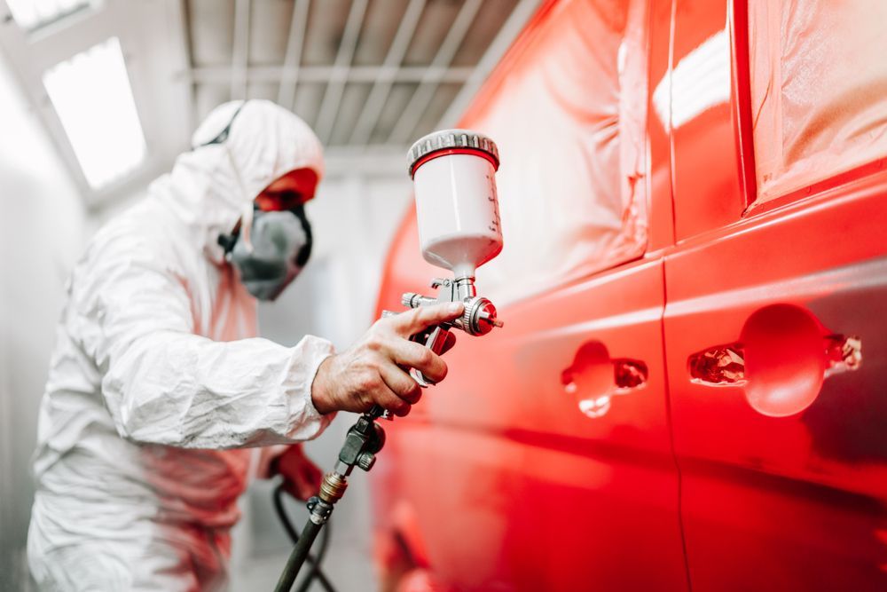 A Man in a Protective Suit is Spray Painting a Red Van — T&C Smash Repairs In Coffs Harbour, NSW