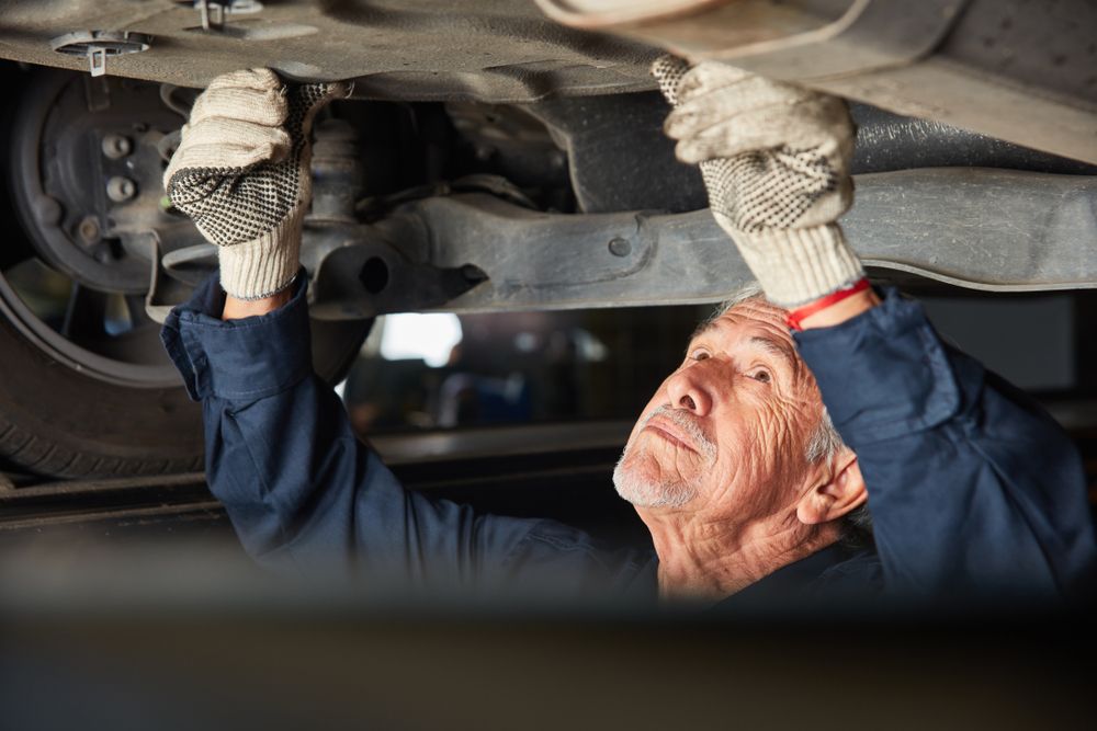 An Older Man is Working Under a Car in a Garage — T&C Smash Repairs In Coffs Harbour, NSW