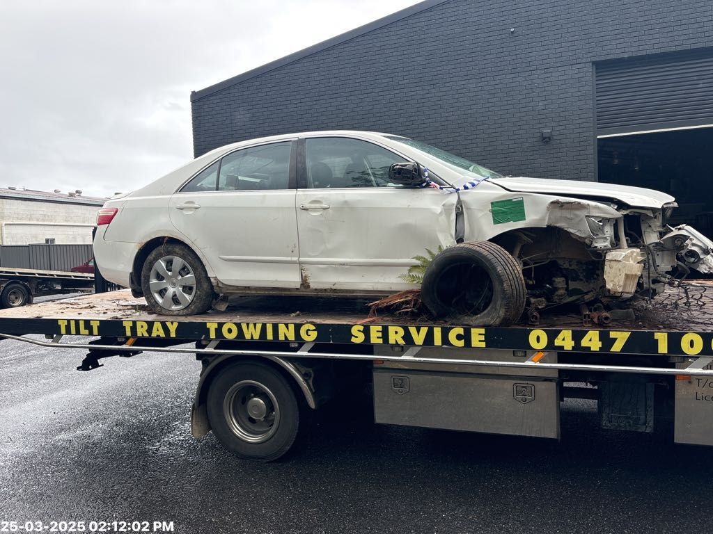 a smashed white car on the back of a tilt tray truck