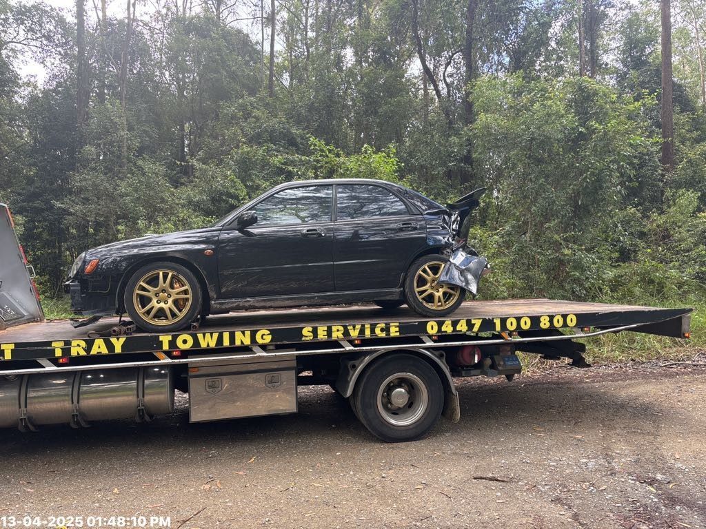 a smashed white car on the back of a tilt tray truck