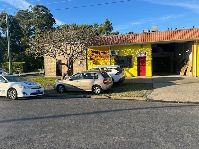 A Yellow Building With a Red Door and a Garage, Cars Parked in Front — T&C Smash Repairs In Coffs Harbour, NSW