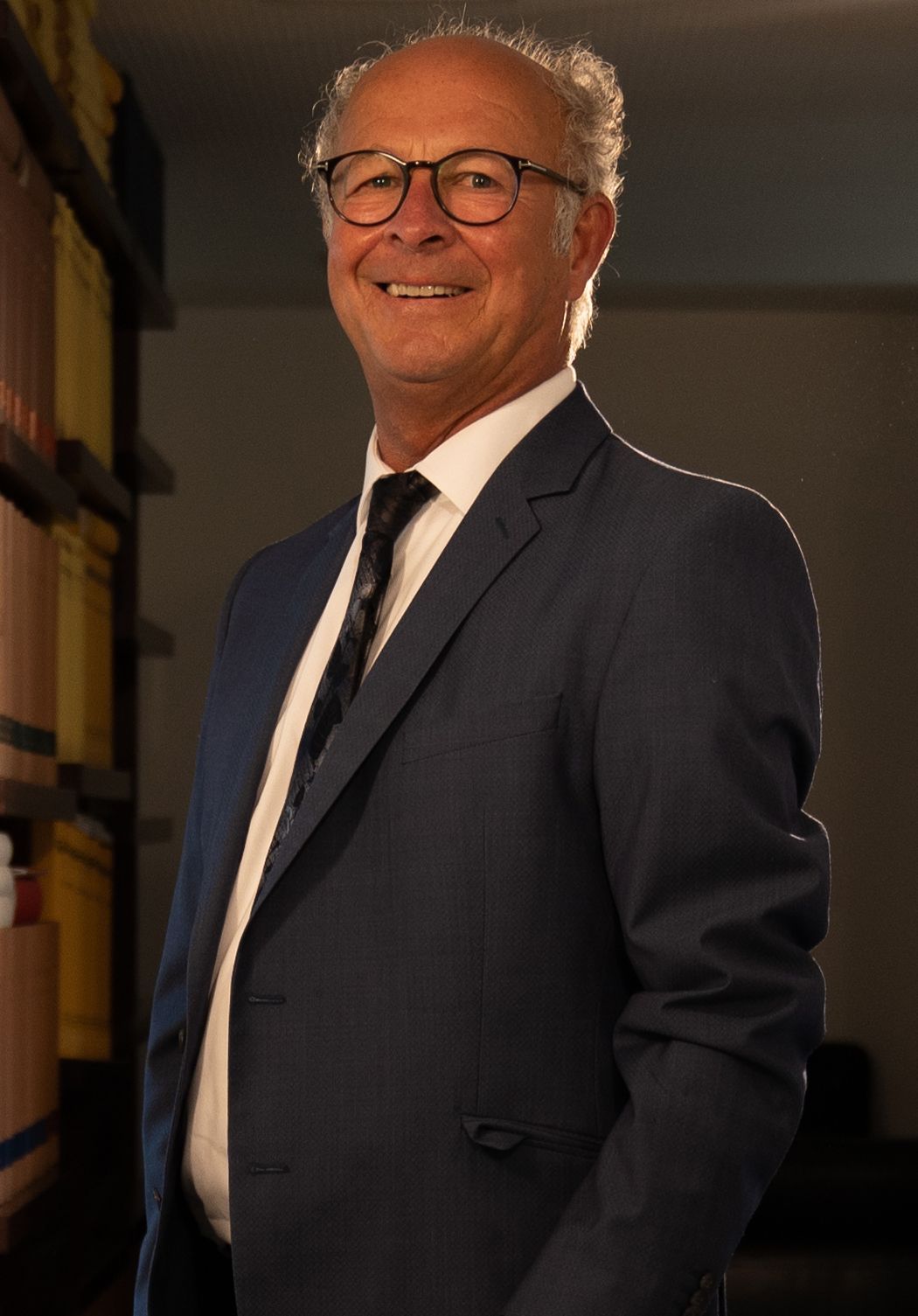 A man in a suit and tie is standing in front of a bookshelf.