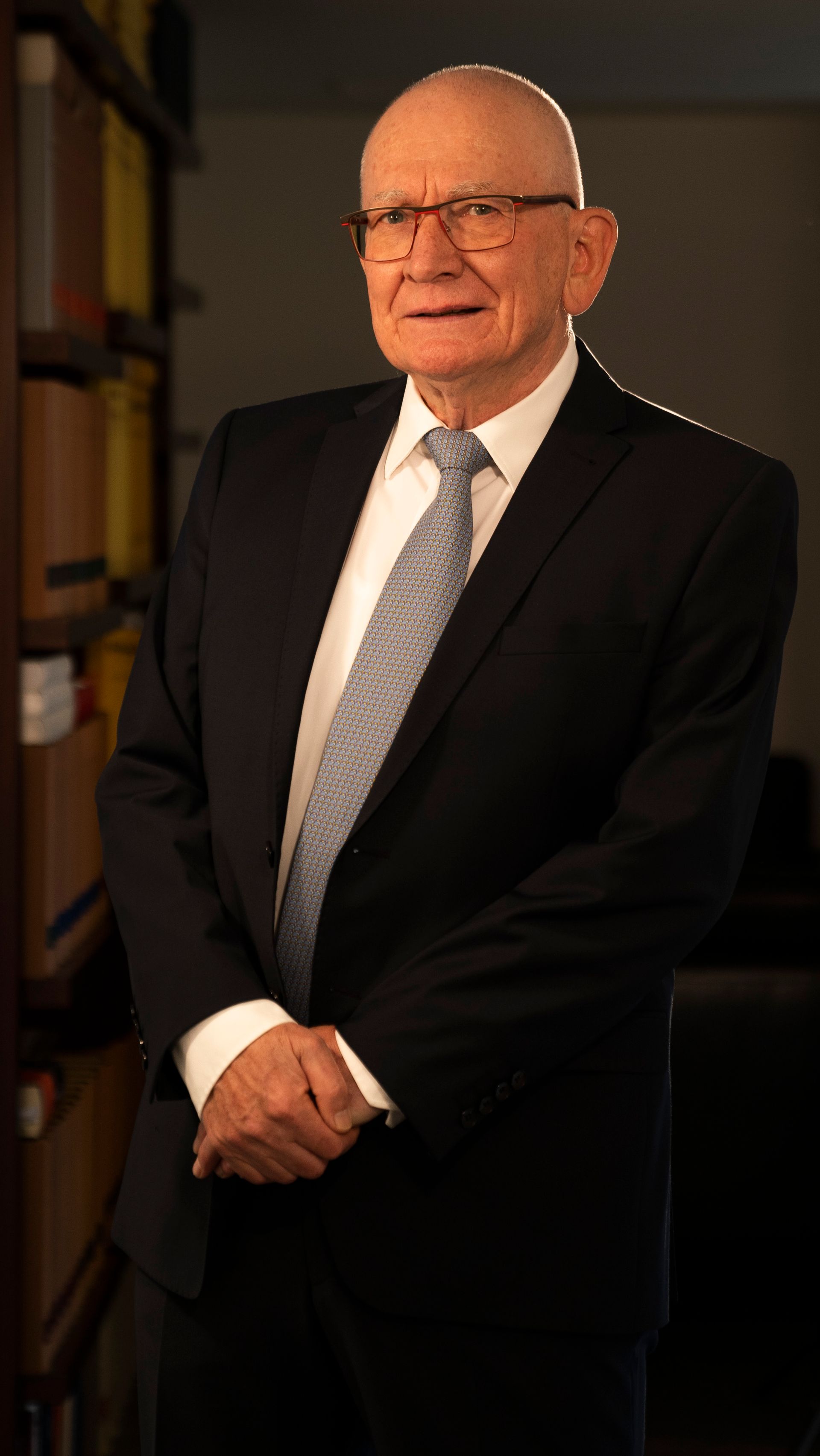 A man in a suit and tie is standing in front of a bookshelf.