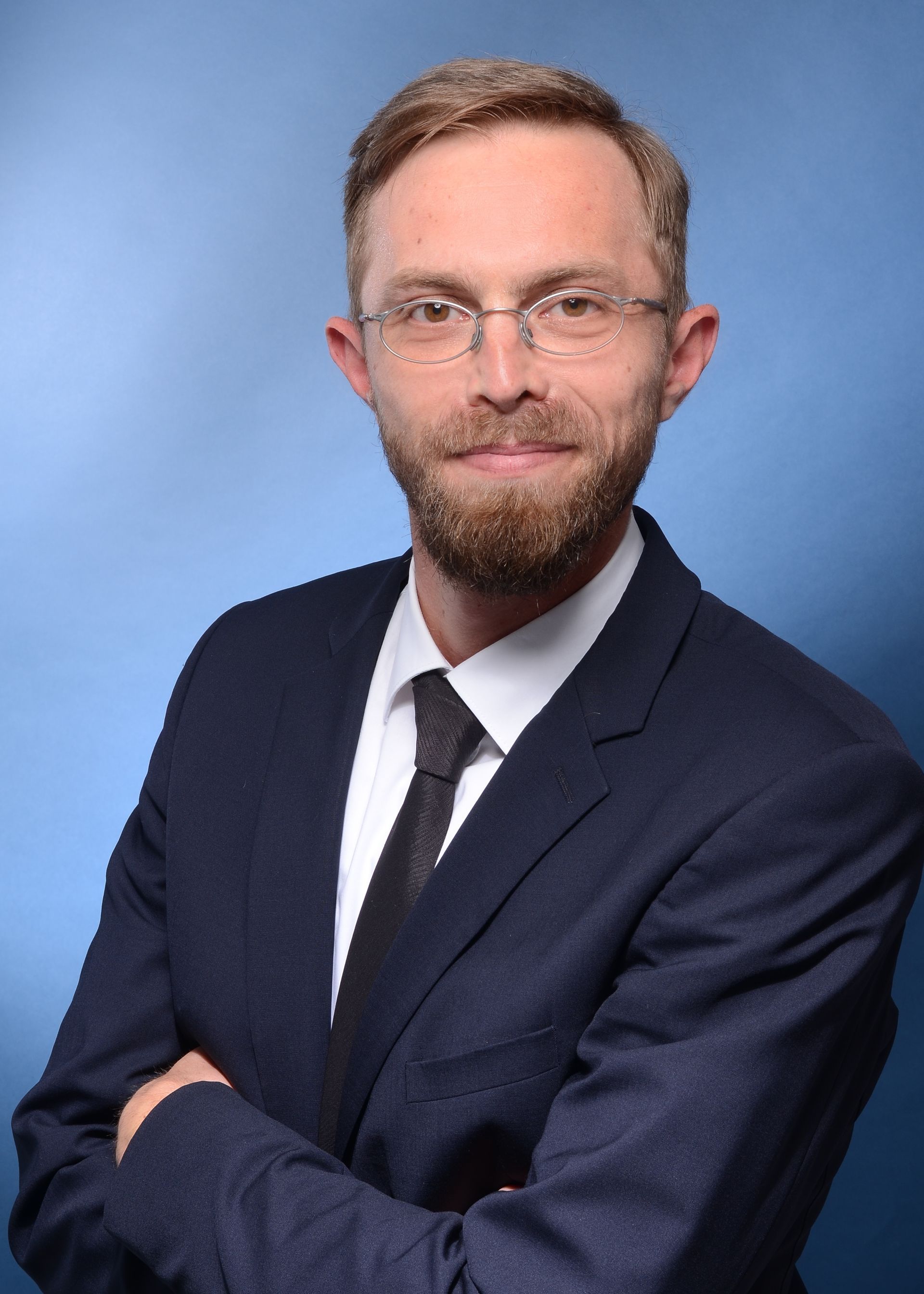 A man in a suit and tie is standing in front of a bookshelf.
