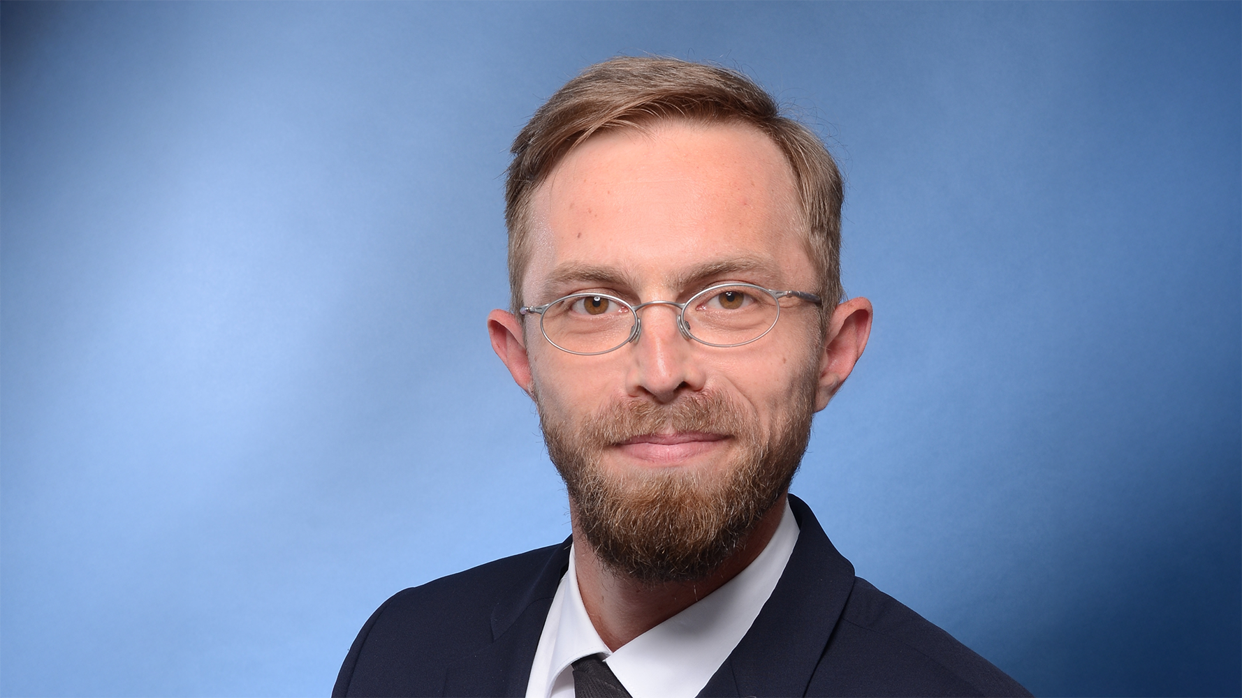 Ein Mann mit Bart und Brille trägt Anzug und Krawatte.