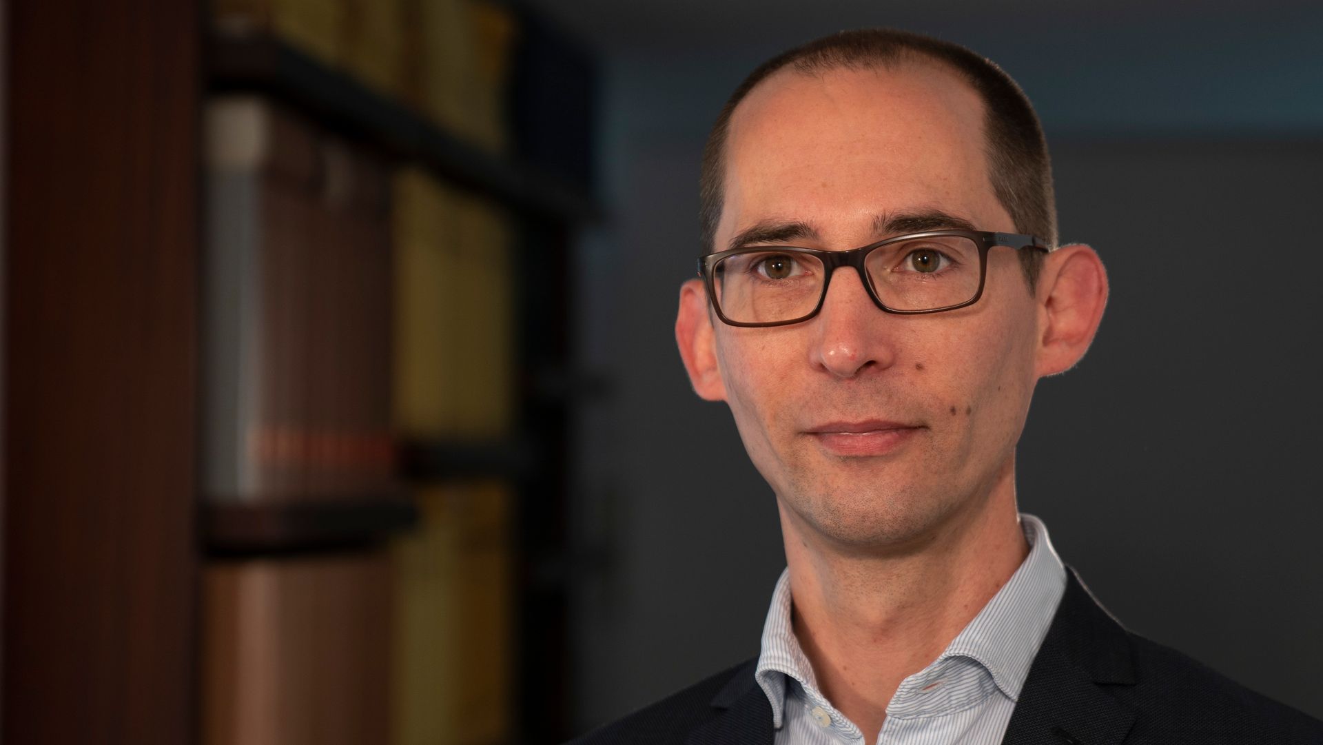 A man wearing glasses and a suit is looking at the camera.