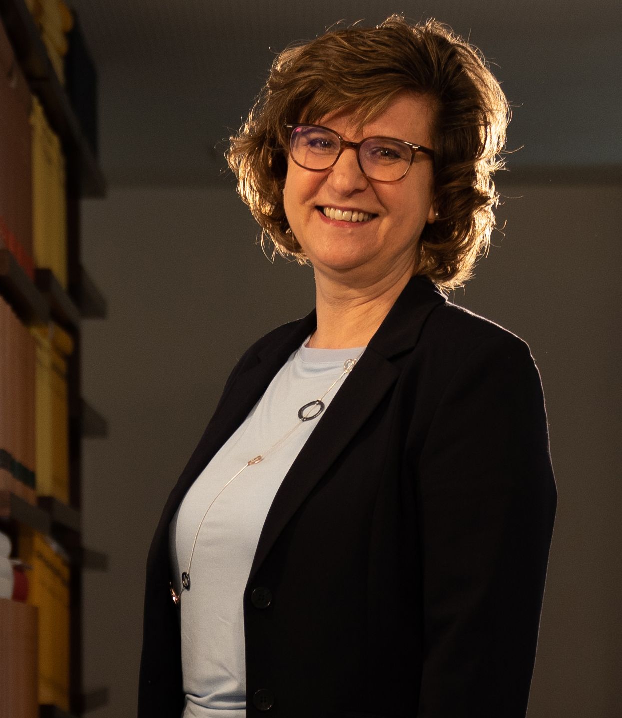 A woman wearing glasses and a black jacket is smiling for the camera.