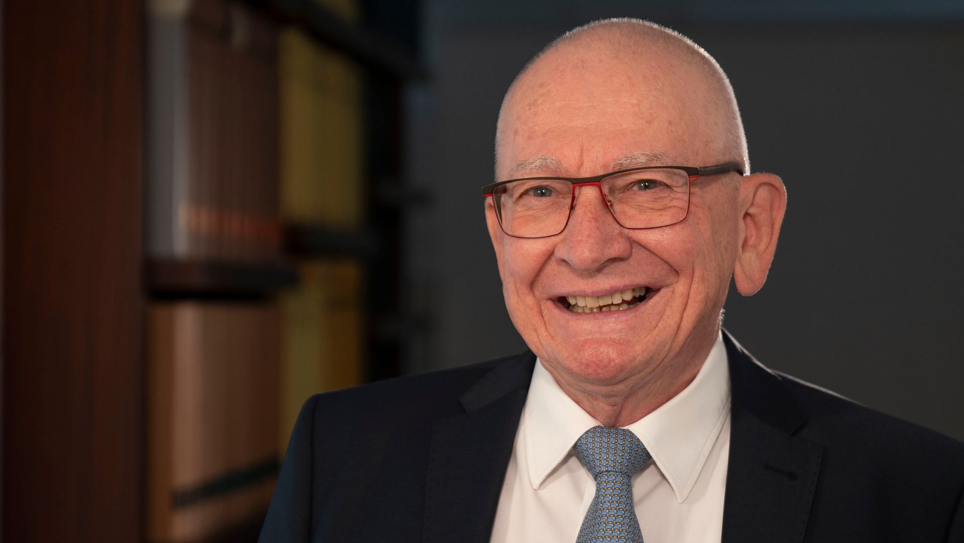 An older man wearing glasses and a suit is smiling for the camera.