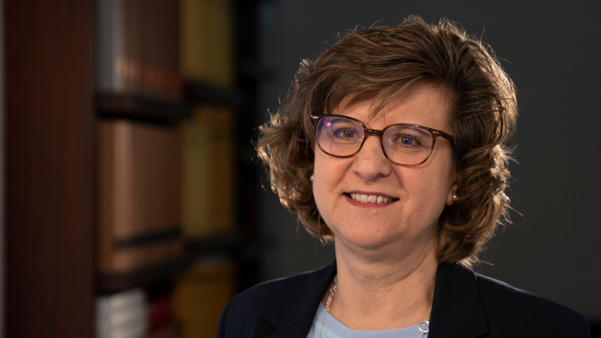 Eine Frau mit Brille und Jacke lächelt in die Kamera.