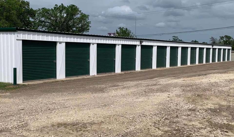 A row of storage units with green doors on a dirt road.
