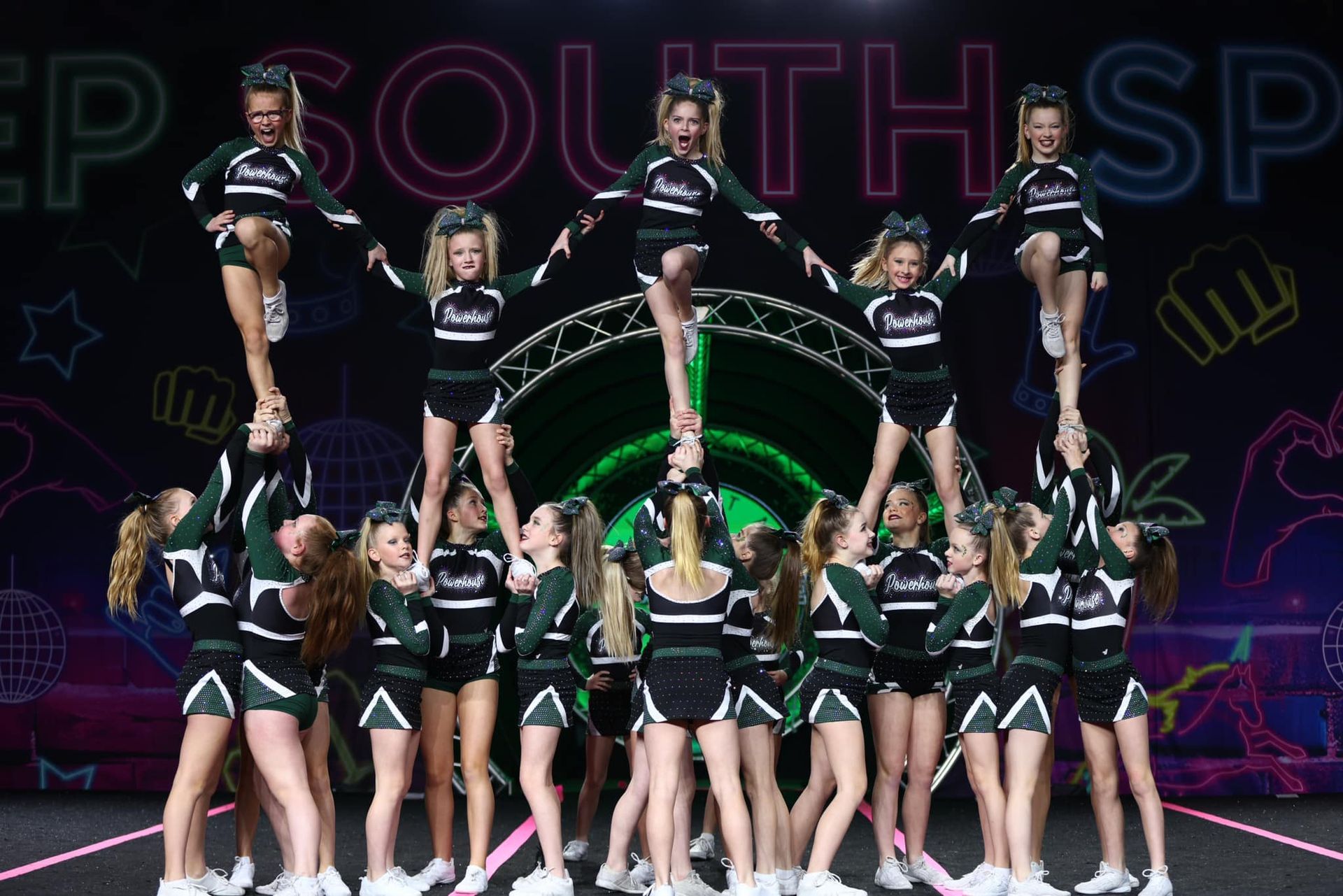 Cheerleaders in black-and-green uniforms perform a stunt onstage at a South Point event