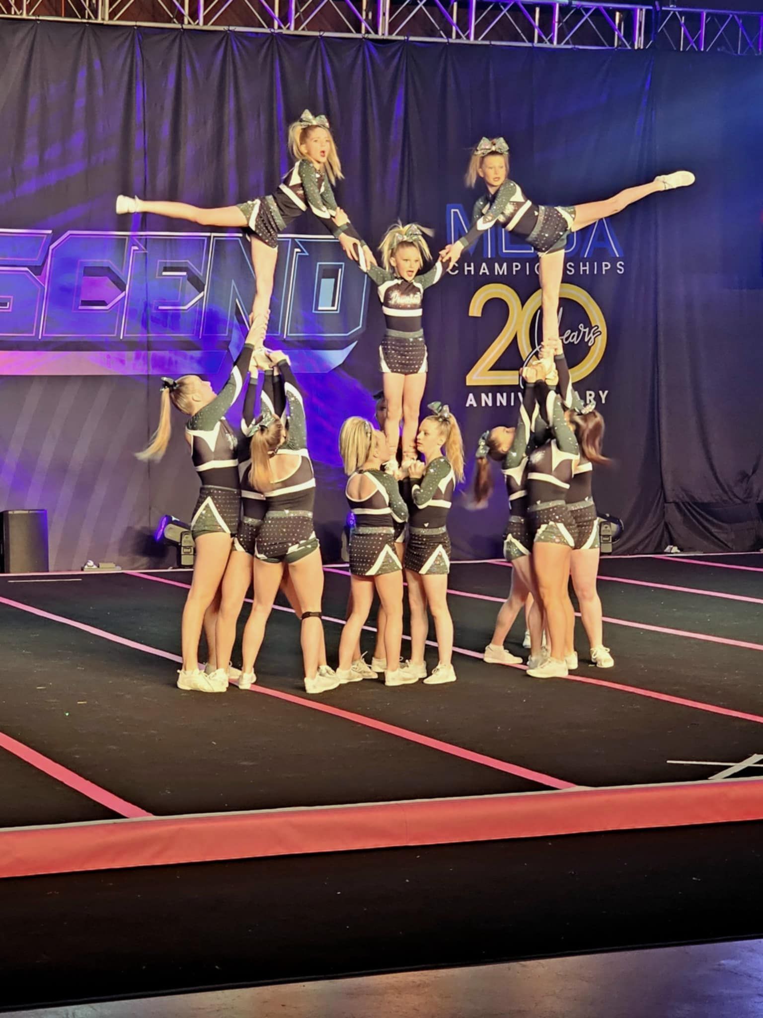 Cheer team performing a pyramid on a competition mat with blue and gold stage backdrop