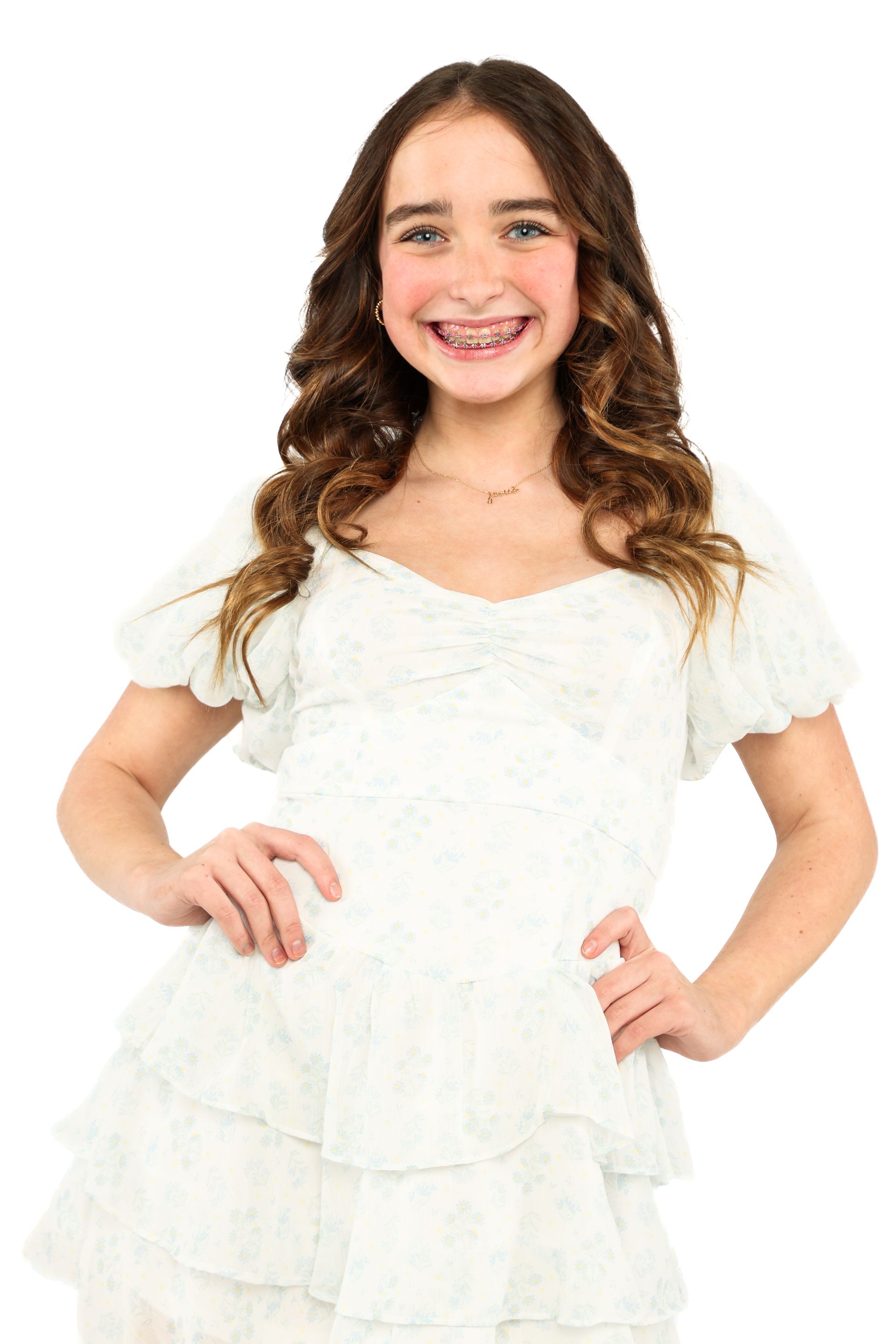 Smiling child in a white dress standing with hands on hips against a white background