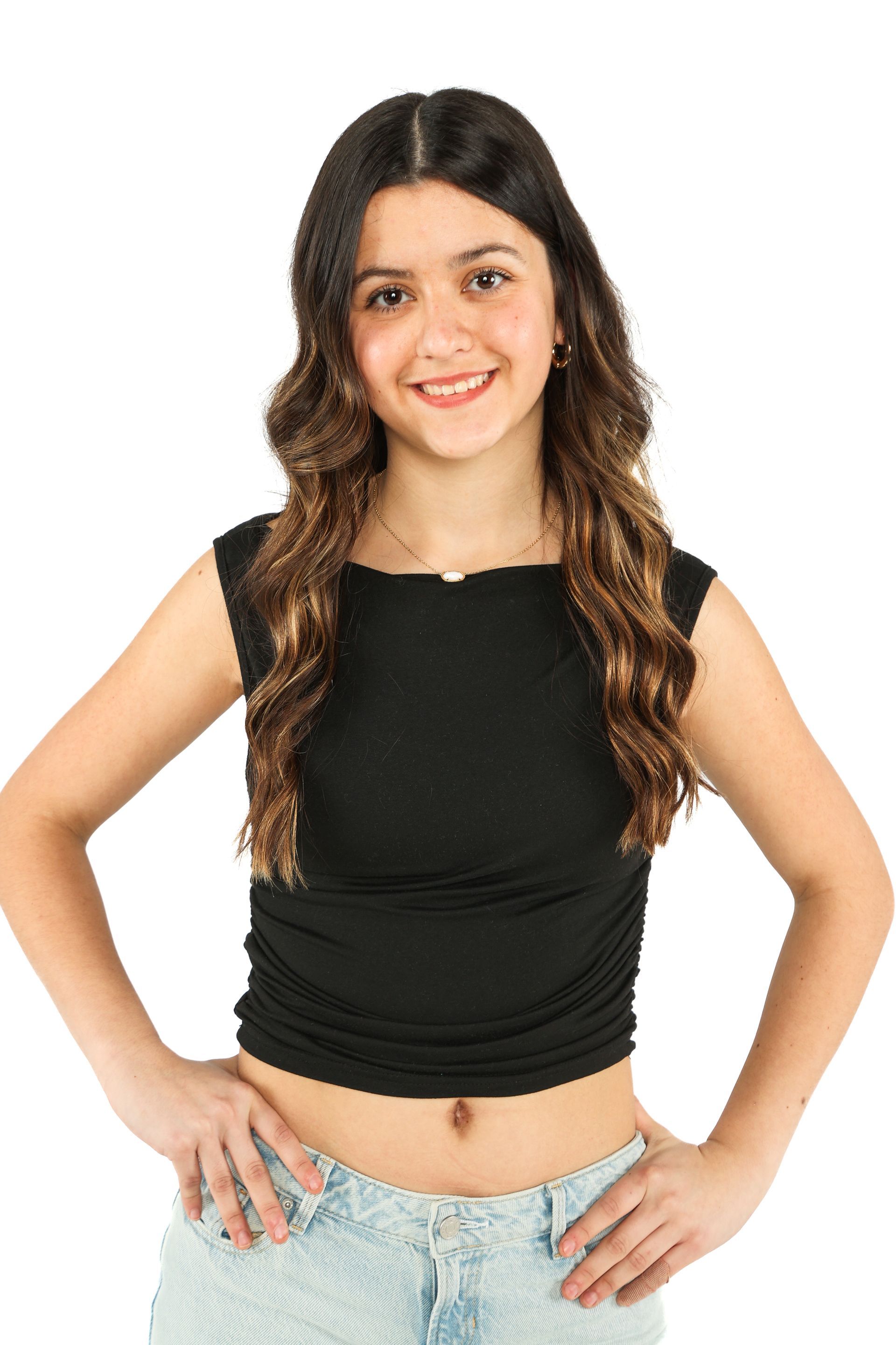 Young woman standing with hands on hips, wearing a black top and light jeans, smiling against a white background