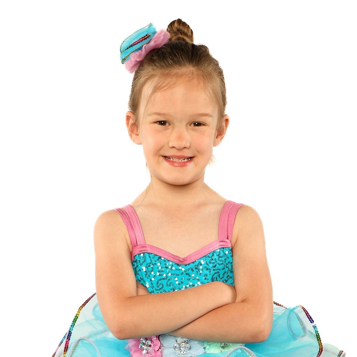 Smiling child in a turquoise and pink dress with arms crossed over a tutu
