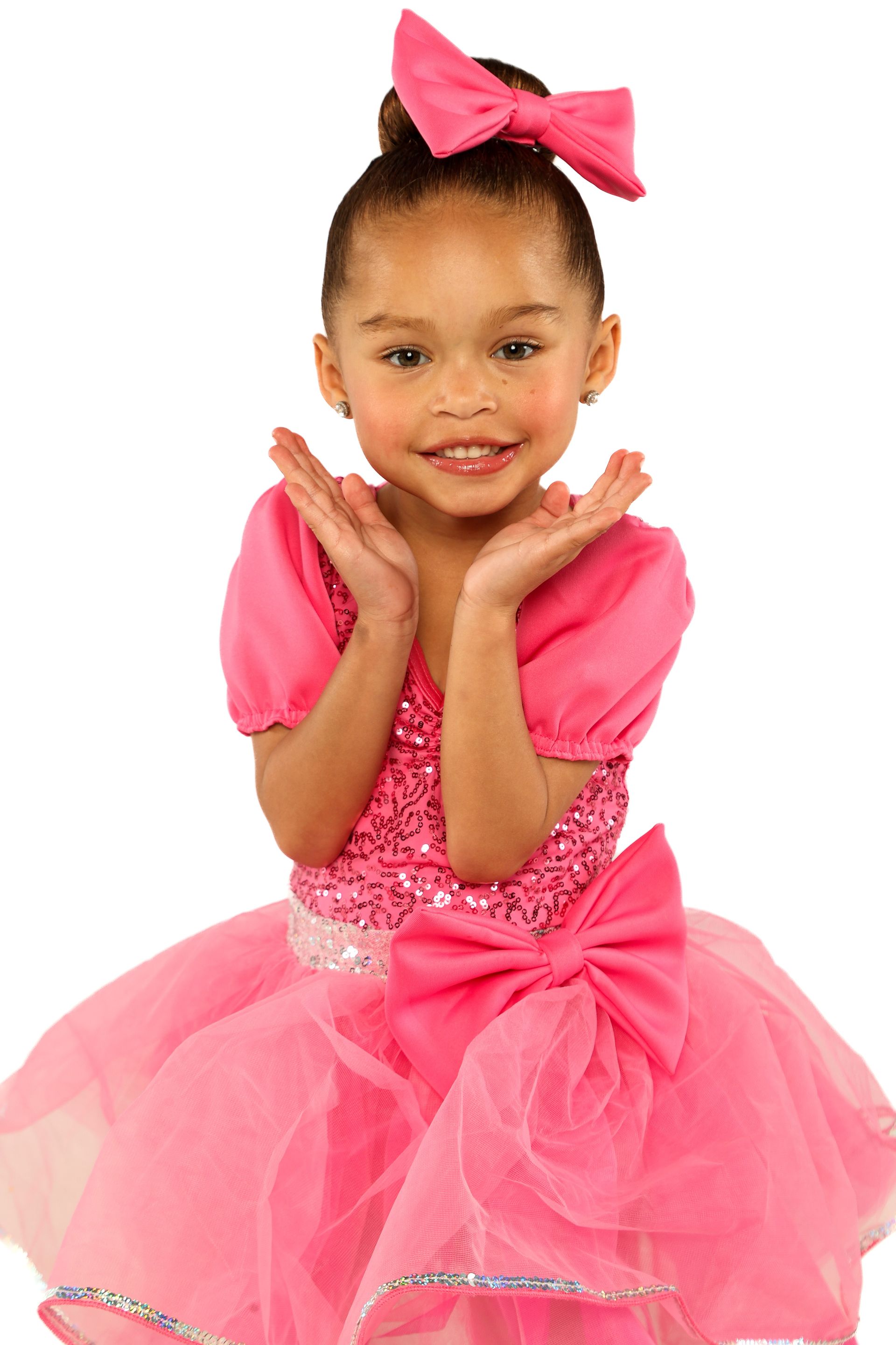 Child in a bright pink dress with a large bow, posing with hands under chin against a white background